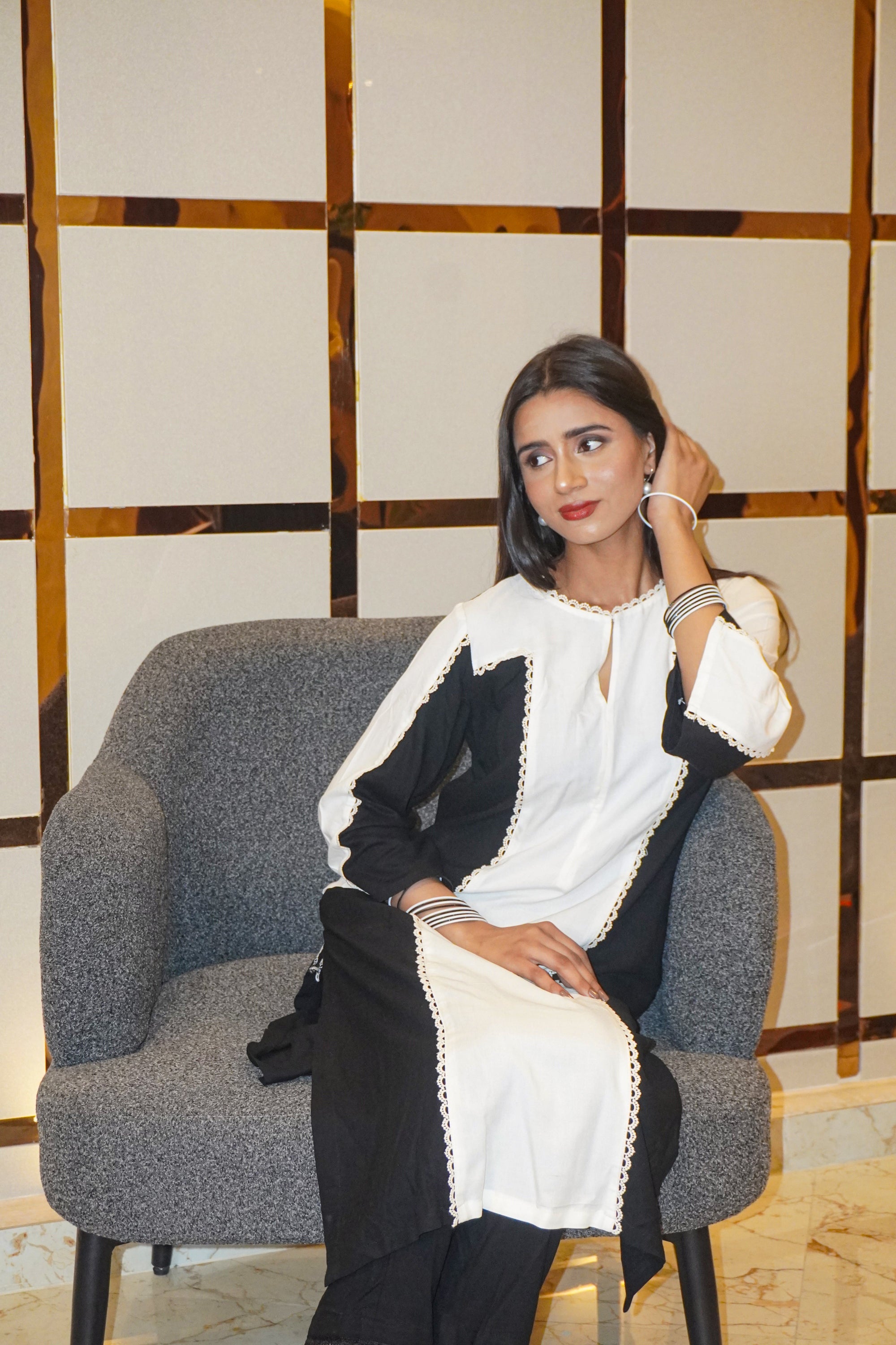 Woman sitting on a gray chair wearing a black and white outfit with a decorative pattern.