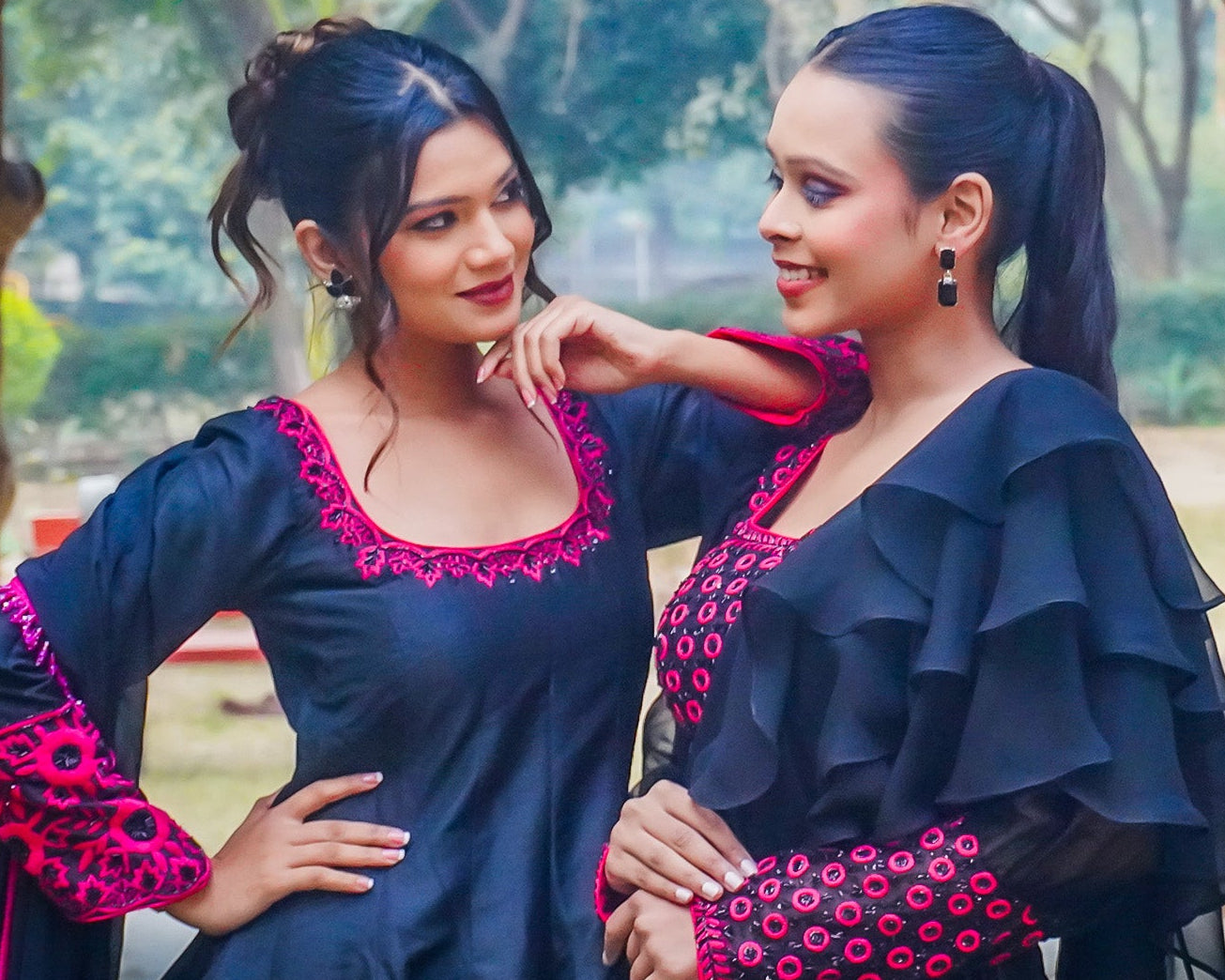 Two women in traditional black and pink dresses sitting outdoors.